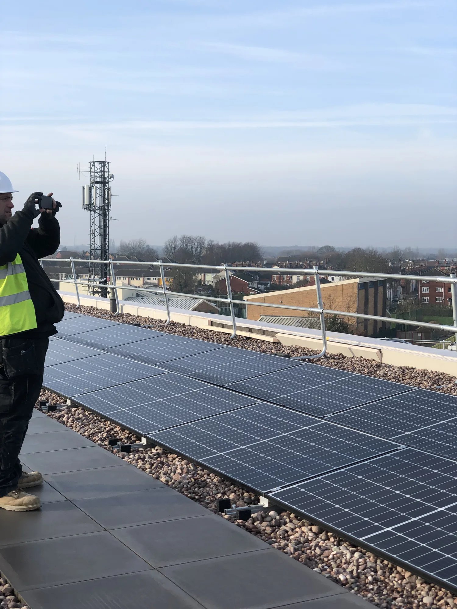 Engineer in hi-vis at roof level beside a ballasted solar array